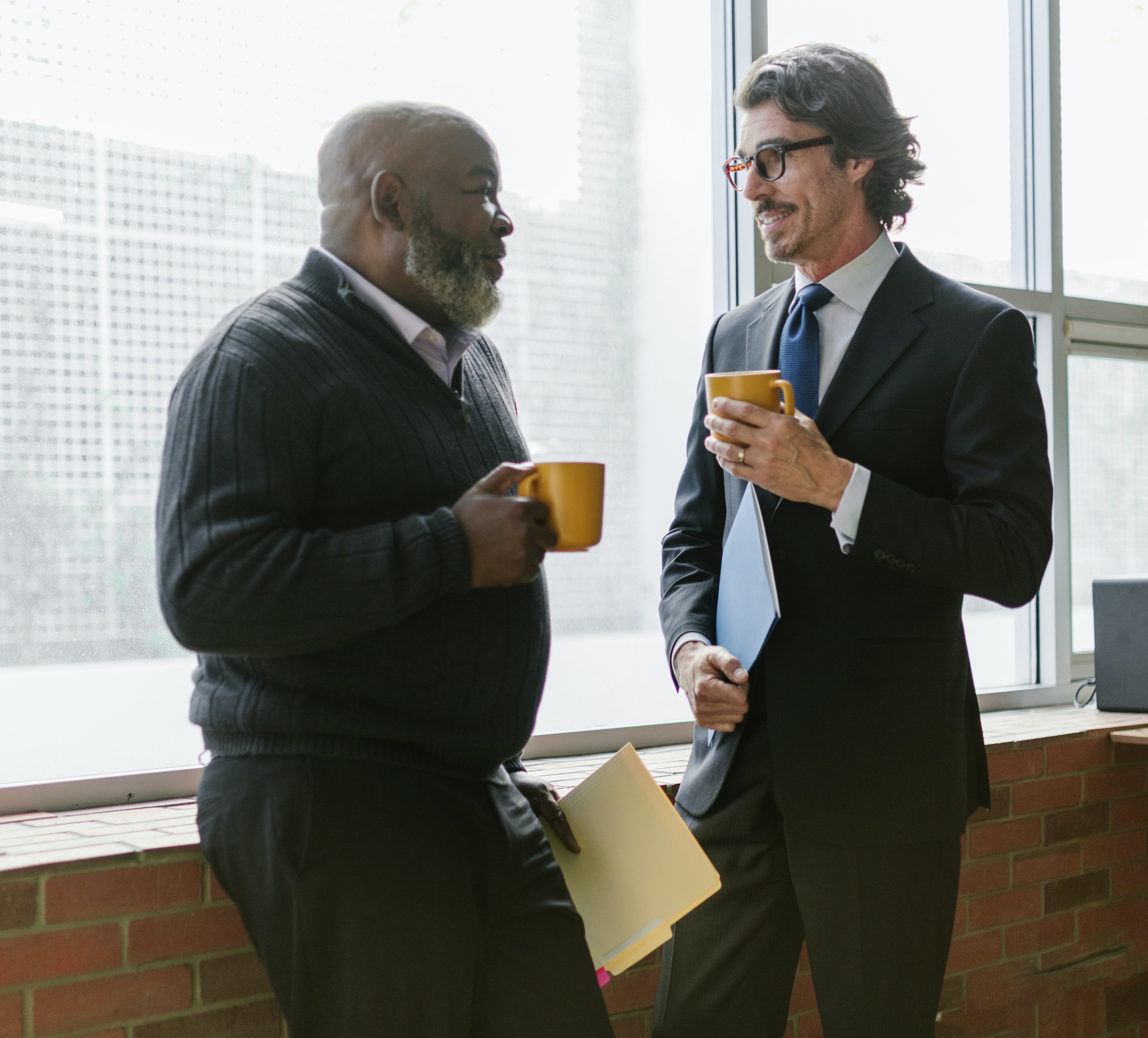 Two businessmen standing next to a window talking.